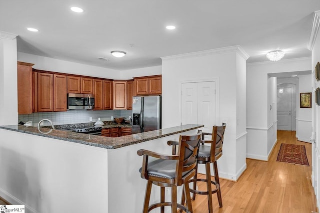 kitchen with kitchen peninsula, dark stone countertops, decorative backsplash, appliances with stainless steel finishes, and light wood-type flooring