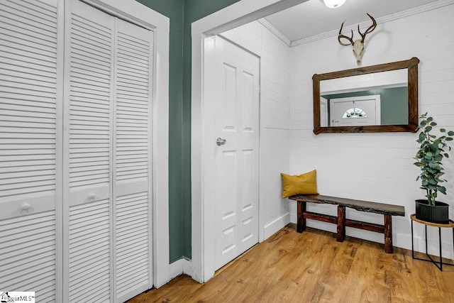 hallway featuring wood walls, light hardwood / wood-style floors, and crown molding