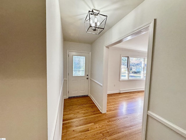 doorway featuring an inviting chandelier, light wood-type flooring, and ornamental molding