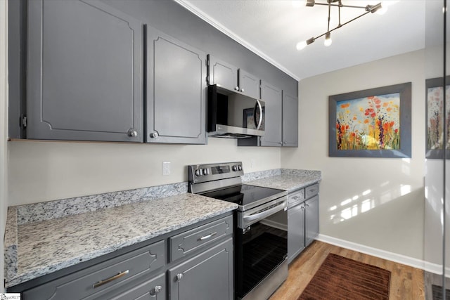 kitchen with gray cabinetry, light stone countertops, light wood-type flooring, ornamental molding, and stainless steel appliances