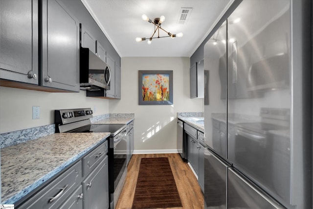 kitchen with a chandelier, stainless steel appliances, light hardwood / wood-style flooring, and light stone countertops