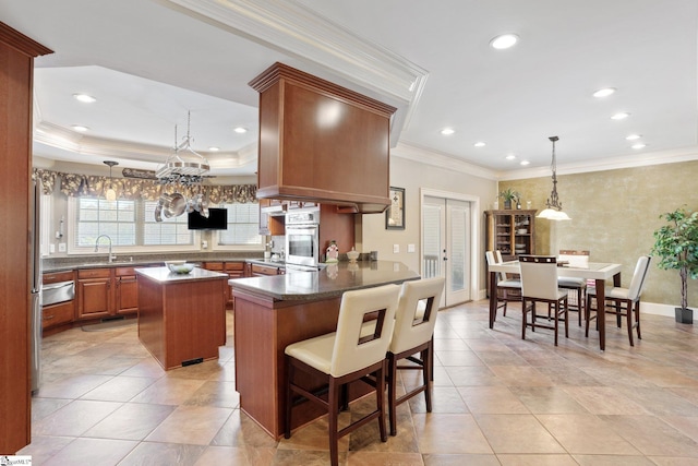 kitchen with crown molding, hanging light fixtures, a kitchen island, kitchen peninsula, and a breakfast bar area