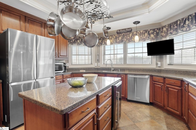 kitchen featuring stainless steel appliances, a tray ceiling, sink, pendant lighting, and a kitchen island