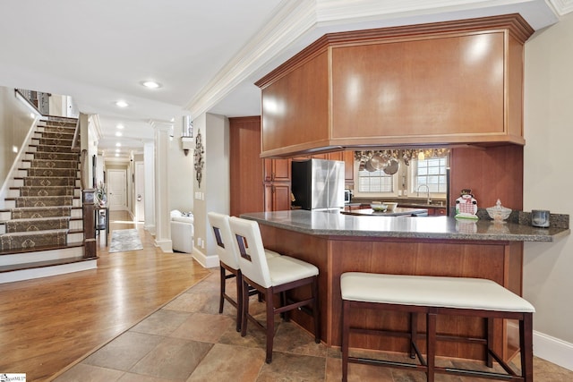 kitchen featuring kitchen peninsula, light wood-type flooring, stainless steel refrigerator, and ornamental molding