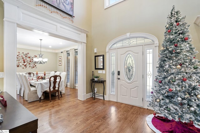 foyer entrance with a chandelier, wood-type flooring, a wealth of natural light, and ornamental molding