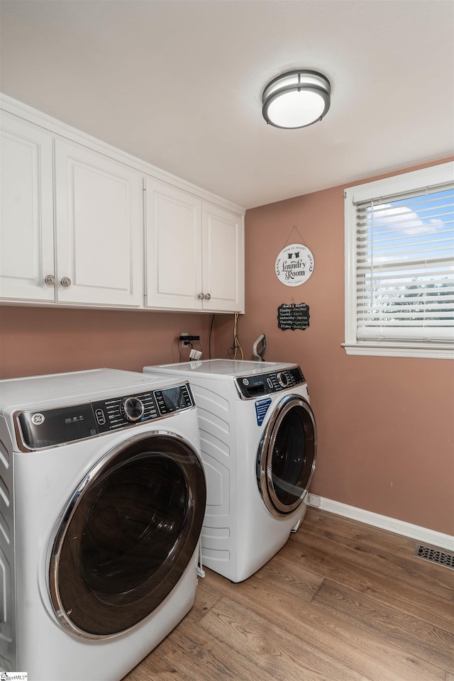 laundry area featuring washing machine and dryer, cabinets, and light hardwood / wood-style floors