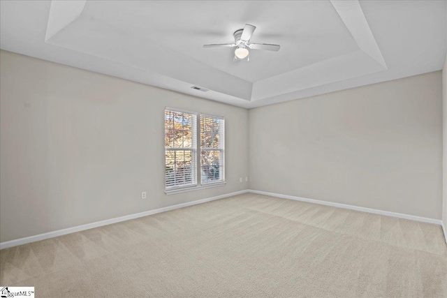 spare room with a raised ceiling, light carpet, and ceiling fan