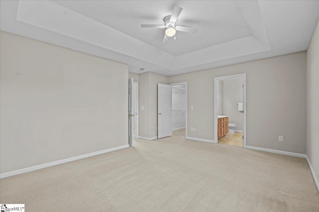 unfurnished bedroom featuring ensuite bath, ceiling fan, a raised ceiling, a walk in closet, and a closet