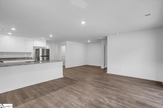 kitchen with light stone countertops, stainless steel fridge, white cabinets, and hardwood / wood-style flooring