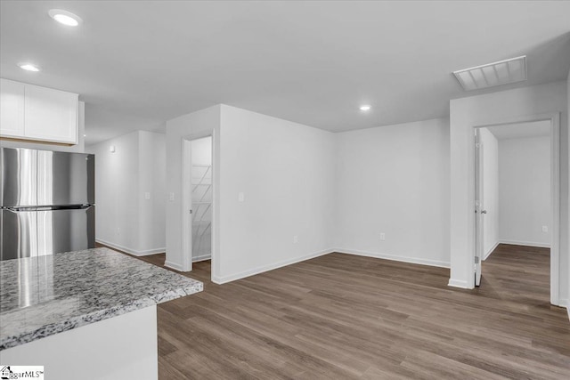 kitchen with white cabinets, stainless steel fridge, light stone counters, and wood-type flooring