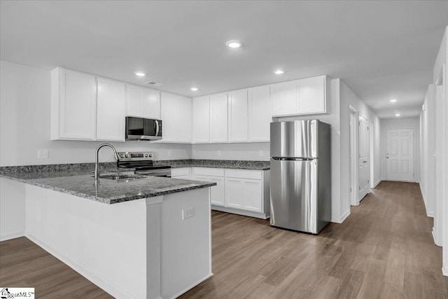 kitchen featuring appliances with stainless steel finishes, dark stone counters, sink, hardwood / wood-style flooring, and white cabinets