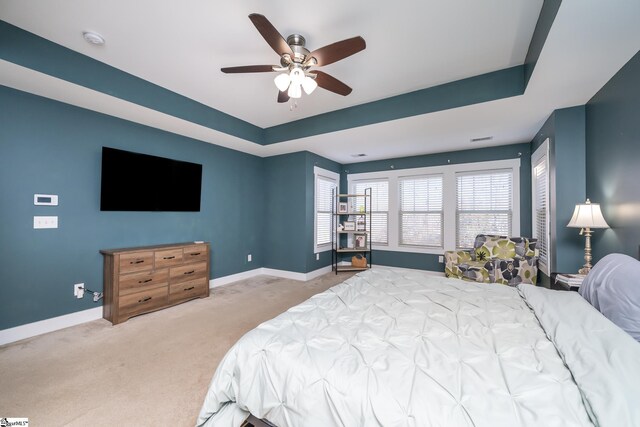 carpeted bedroom with ceiling fan and a raised ceiling