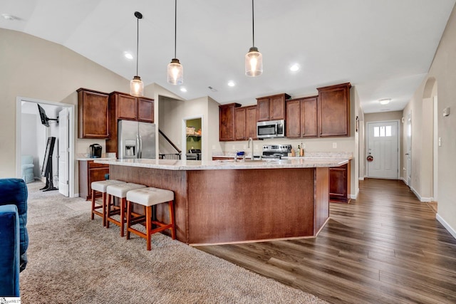 kitchen featuring pendant lighting, stainless steel appliances, a kitchen island with sink, and lofted ceiling