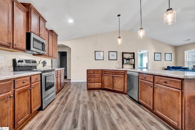 kitchen with hanging light fixtures, stainless steel appliances, vaulted ceiling, and light wood-type flooring