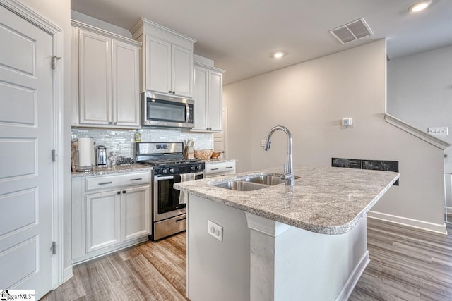 kitchen with white cabinetry, sink, a kitchen island with sink, appliances with stainless steel finishes, and light wood-type flooring