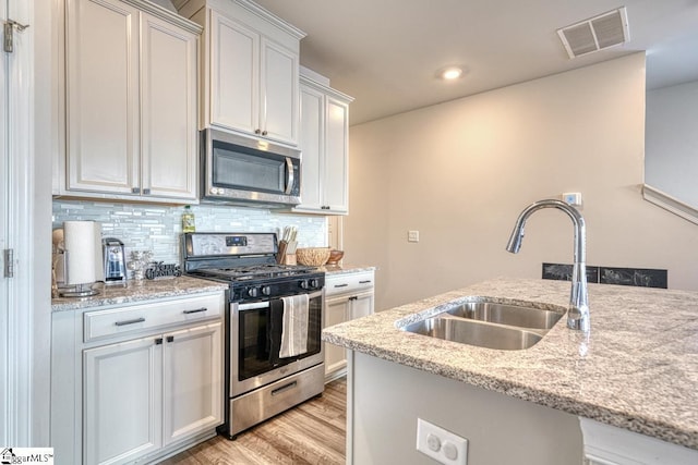 kitchen with sink, stainless steel appliances, light stone counters, white cabinets, and light wood-type flooring