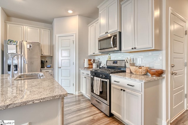 kitchen featuring light stone counters, white cabinetry, light wood-type flooring, and appliances with stainless steel finishes