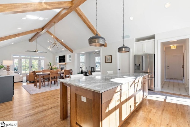 kitchen featuring light stone counters, high quality fridge, a center island, white cabinetry, and hanging light fixtures