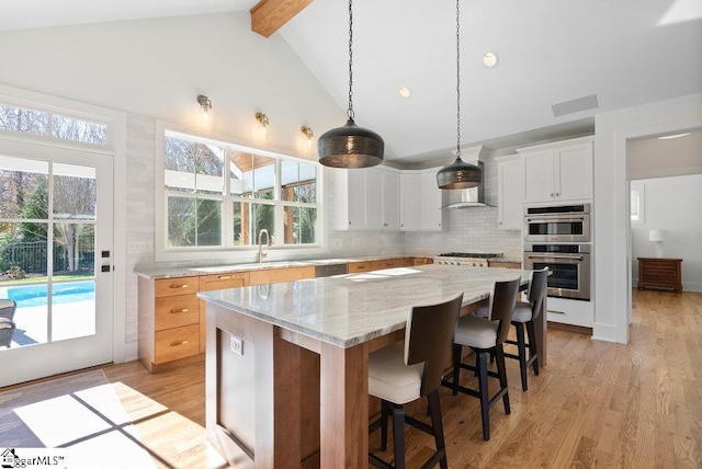 kitchen featuring light stone counters, decorative light fixtures, white cabinets, light hardwood / wood-style floors, and a kitchen island