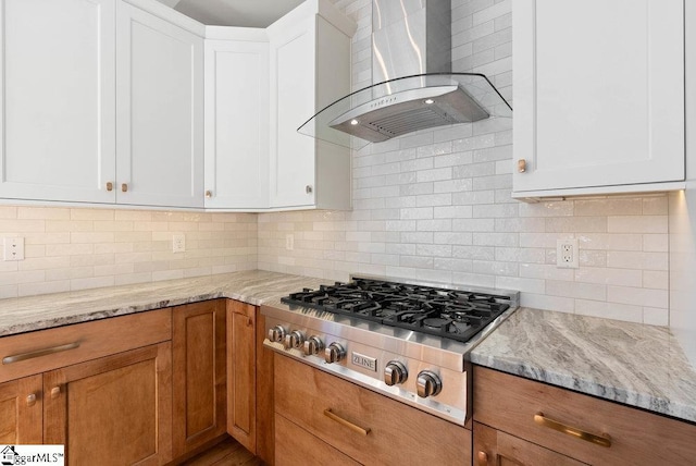 kitchen with white cabinets, stainless steel gas stovetop, decorative backsplash, and wall chimney range hood