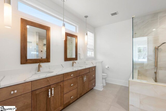 bathroom with tiled shower, vanity, and a healthy amount of sunlight