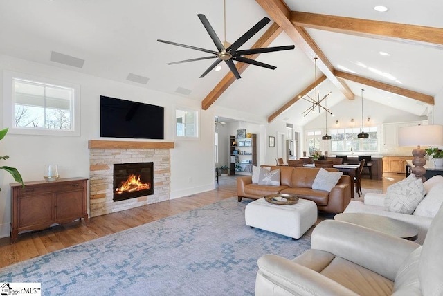 living room featuring ceiling fan with notable chandelier, light wood-type flooring, a stone fireplace, and a wealth of natural light