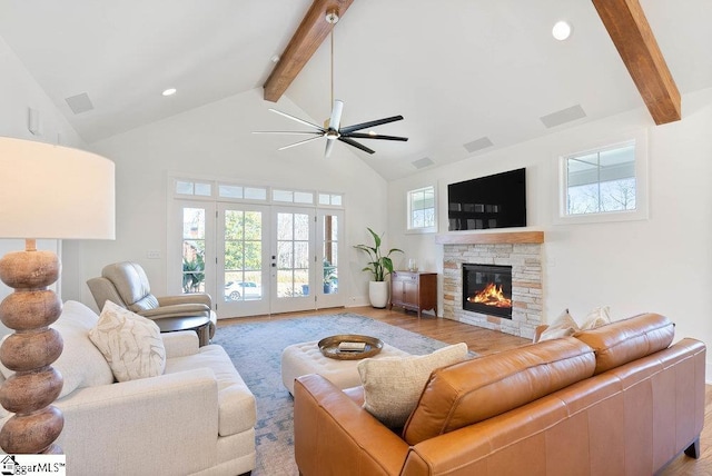 living room featuring ceiling fan, french doors, light hardwood / wood-style flooring, beamed ceiling, and a fireplace