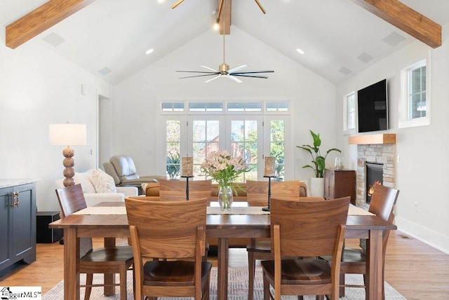 dining room with beamed ceiling, light hardwood / wood-style floors, a fireplace, and high vaulted ceiling