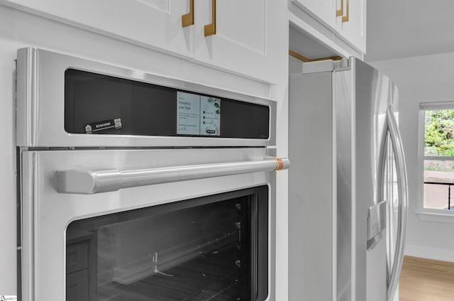 interior details featuring white cabinetry, light hardwood / wood-style floors, and appliances with stainless steel finishes