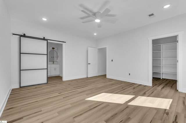 unfurnished bedroom with light hardwood / wood-style floors, ceiling fan, a barn door, and a walk in closet