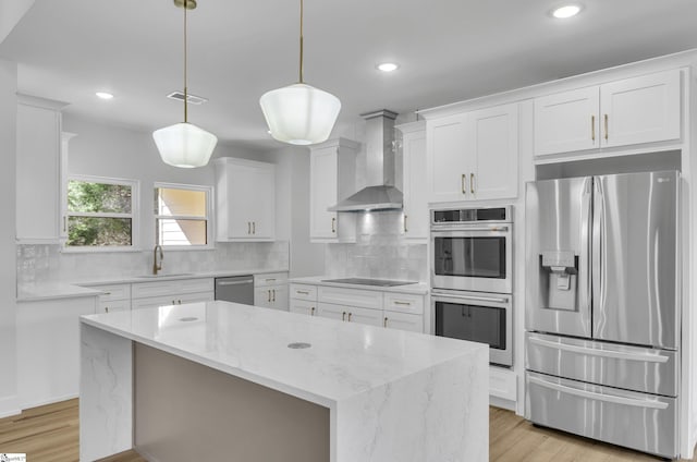 kitchen with wall chimney exhaust hood, stainless steel appliances, white cabinets, a kitchen island, and hanging light fixtures