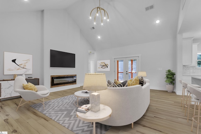 living room with an inviting chandelier, french doors, high vaulted ceiling, and light hardwood / wood-style flooring