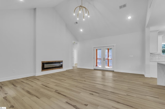 unfurnished living room featuring french doors, an inviting chandelier, high vaulted ceiling, heating unit, and light hardwood / wood-style floors