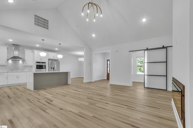 unfurnished living room with a chandelier, a barn door, light hardwood / wood-style floors, and high vaulted ceiling