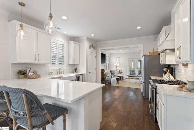 kitchen featuring white cabinetry, dark wood-type flooring, hanging light fixtures, stainless steel appliances, and a kitchen breakfast bar