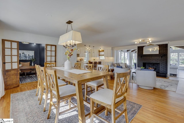 dining space with a brick fireplace, french doors, a chandelier, and light wood-type flooring