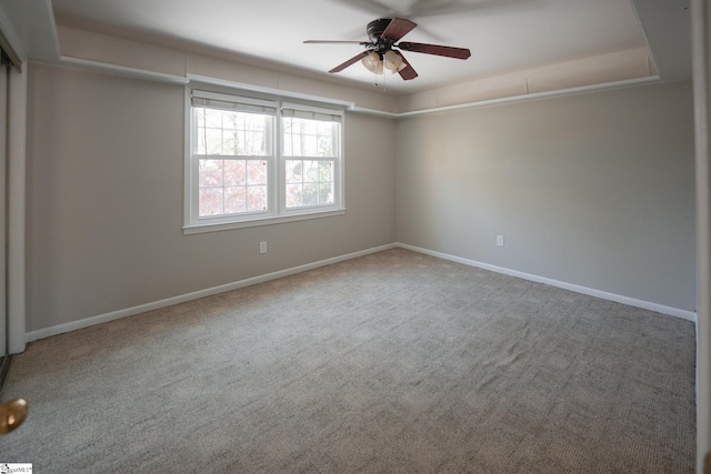 carpeted spare room with a raised ceiling and ceiling fan