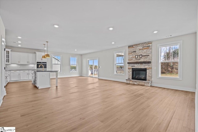 unfurnished living room featuring a stone fireplace, a wealth of natural light, light hardwood / wood-style flooring, and sink