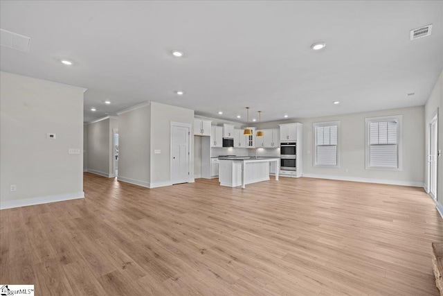 unfurnished living room with sink, light wood-type flooring, and ornamental molding