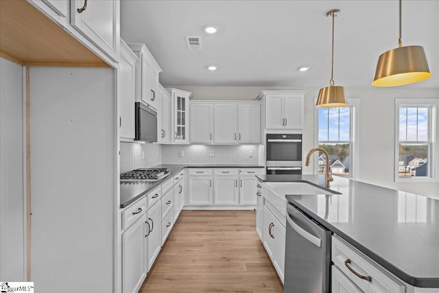 kitchen featuring sink, hanging light fixtures, light hardwood / wood-style flooring, white cabinets, and appliances with stainless steel finishes