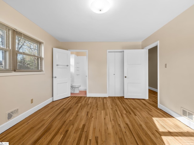 unfurnished bedroom featuring ensuite bath, a closet, and light wood-type flooring