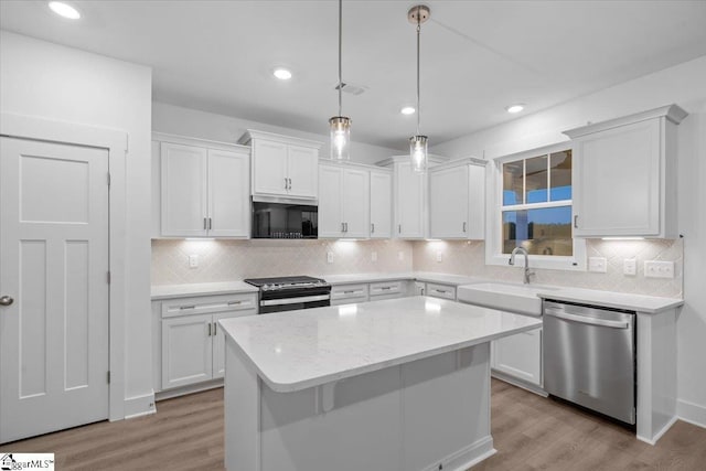 kitchen featuring light wood-type flooring, stainless steel appliances, sink, white cabinets, and a kitchen island