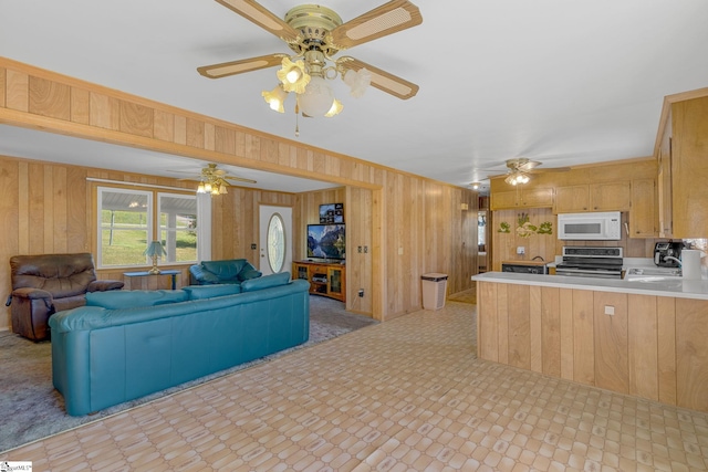 kitchen with sink, wooden walls, light brown cabinetry, stainless steel range, and kitchen peninsula