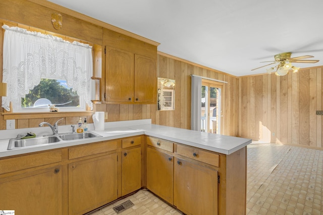 kitchen with ceiling fan, wood walls, kitchen peninsula, and sink