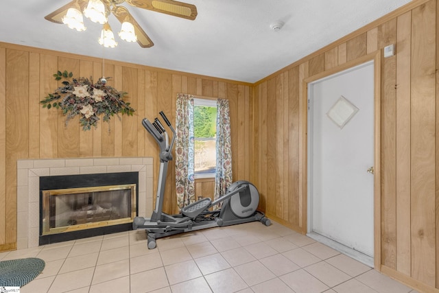 workout room with a tiled fireplace, wooden walls, ceiling fan, and light tile patterned flooring