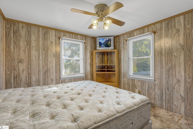 carpeted bedroom featuring ceiling fan, wood walls, ornamental molding, and multiple windows