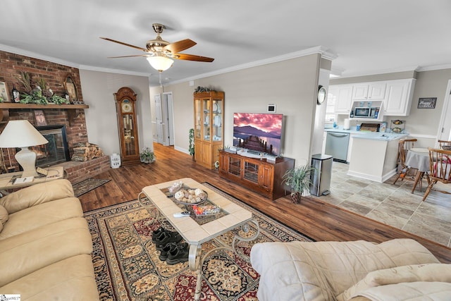 living room featuring ceiling fan, light hardwood / wood-style floors, crown molding, and a fireplace