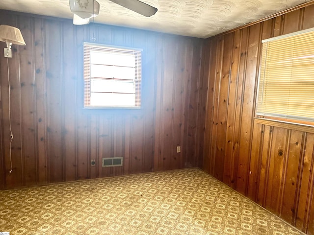 unfurnished room featuring visible vents, wooden walls, and light floors