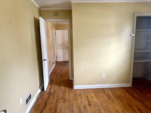 unfurnished bedroom with ornamental molding, wood-type flooring, visible vents, and baseboards