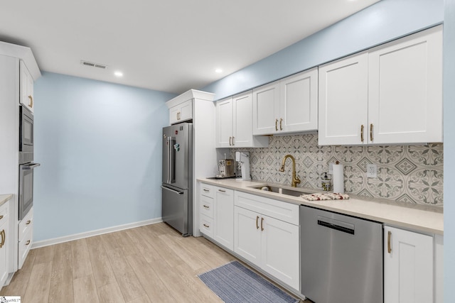 kitchen with white cabinets, decorative backsplash, stainless steel appliances, and light hardwood / wood-style flooring